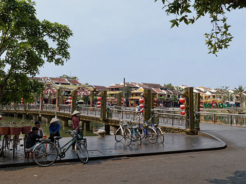 Hoi An, Vietnam - March 23, 2023: The view of buildings and the bridge across the Thu Bon river where bicycles are parked on the other side of the river.