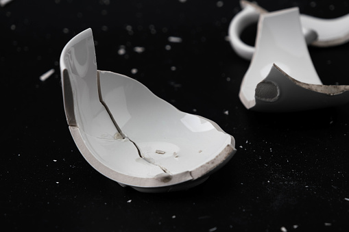 Large white mug with cracks. White cup for tea or soup with cracks isolated on dark background. Broken ceramic cup close up. symbol of divorce or loss