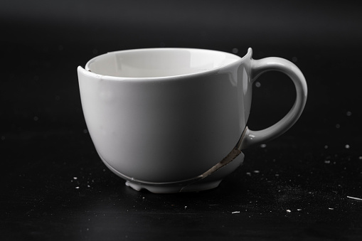 Large white mug with cracks. White cup for tea or soup with cracks isolated on dark background. Broken ceramic cup close up. symbol of divorce or loss
