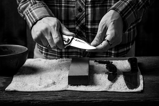 The man using whetstone to sharpening his pocket knife. Pocket knife care and maintenance concept.
