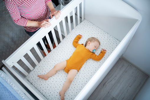 Young mother watching her baby boy sleeping in his crib.