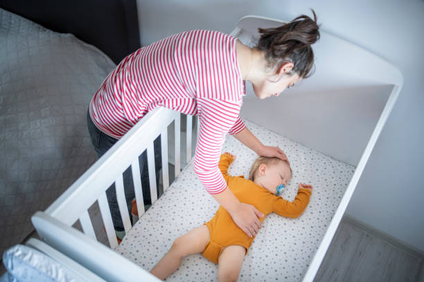 Caring mother putting her baby boy to sleep. Caring young mother putting her baby boy for his nap. crib stock pictures, royalty-free photos & images