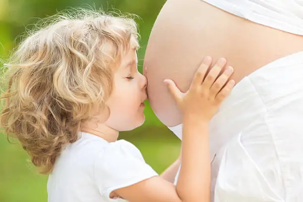 Photo of Child kissing belly of pregnant woman