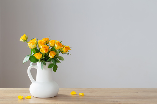 yellow roses in white jug on wooden shelf