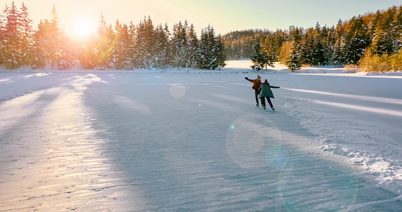 Rear view of couple ice skating on frozen lake during sunset.