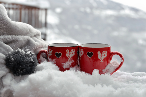 two red mugs with heart shaped on the snow with blanket on  mountain background