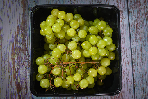 Black basket with a bunch of freshly harvested organic grapes.