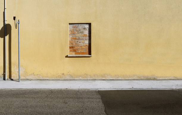 istock Window walled by bricks on a yellow plaster facade. Concrete sidewalk and road in front. 1633121724