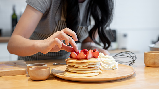 Close-up image of a woman enjoys decorating her pancakes with strawberries while preparing her fancy breakfast in the kitchen.