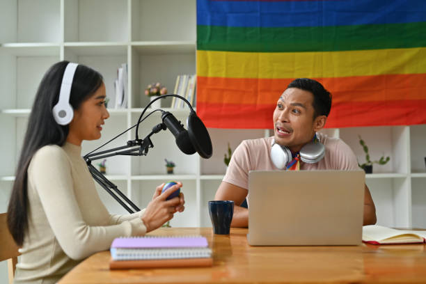presentador de radio gay guapo entrevistando a un invitado en el estudio mientras graba un podcast en vivo en el estudio - gay pride flag audio fotografías e imágenes de stock