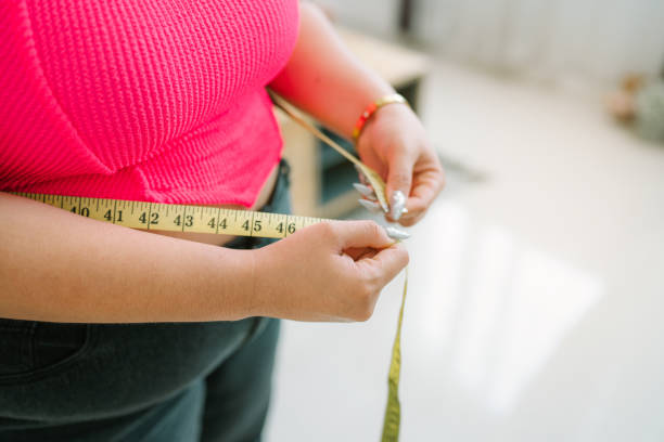 Fat Asian woman want to lose weight with a centimeter Shape up healthy stomach muscle. Fat Asian woman want to lose weight with a centimeter Shape up healthy stomach muscle and diet measuring waist with measure tape after diet weight control. pudgy woman pictures stock pictures, royalty-free photos & images
