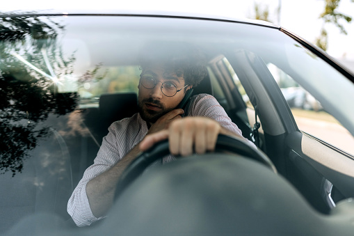 Young casually clothed man talking on a smart phone while driving car