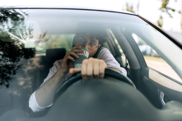 istock Young casually clothed man talking on mobile phone and drinking coffee while driving car 1633254360