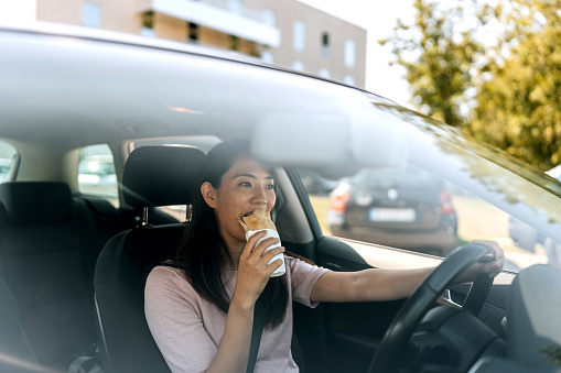 Woman eating sandwich while driving car