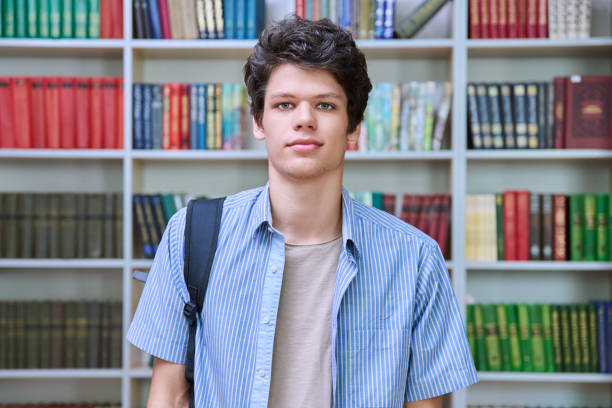 istock Portrait of college student guy with backpack looking at camera inside library of educational building 1633289601
