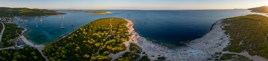 Aerial view of a rocky coastline with turquoise waters and green trees. The beach is located in the Croatian sea.