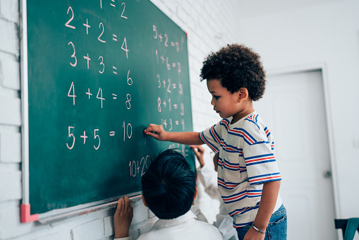 Group of little child standing at chalkboard and writing math formula on blackboard in classroom at school, education concept.