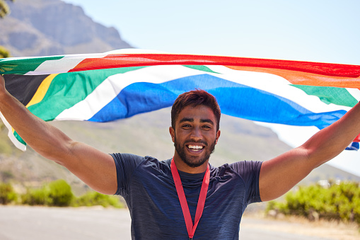 Runner, winner and portrait of happy man with flag on road for fitness goal, winning or running race. Sports champion, proud South African or excited athlete with competition victory or success