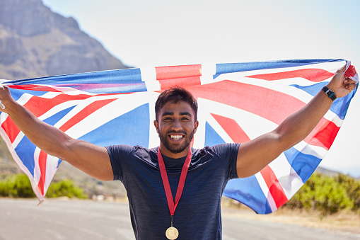 Race, winner and portrait of happy man with flag on road for fitness goal, success or running competition. Proud champion runner, winning or excited British athlete with victory or gold medal in UK