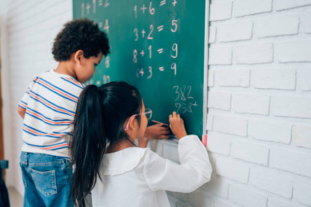 istock Group of little child standing at chalkboard and writing math formula on blackboard in classroom at school. 1633303091