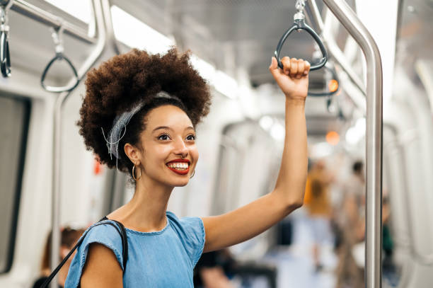 istock Cheerful young ethnic woman standing and holding handle while riding in subway train 1633307843