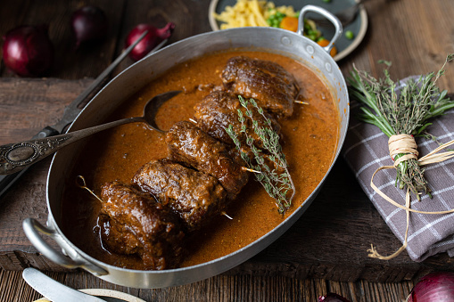 Traditional german sunday or holiday meat dish with oven braised and stuffed beef roulades in a delicious brown gravy. Served ready to eat in a old fashioned roasting pan on wooden table. Top view