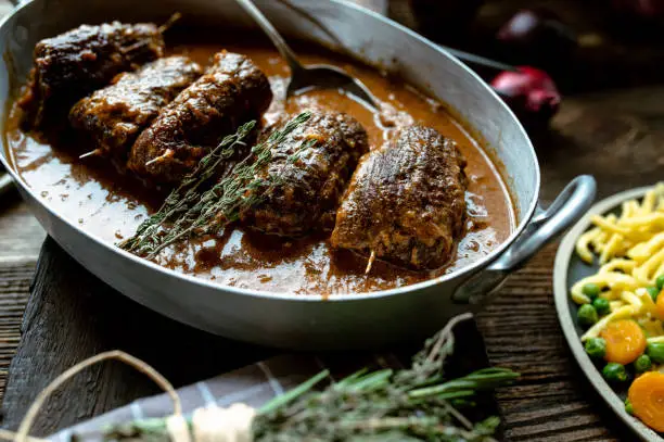 Homemade traditional german oven braised beef roulades with delicious brown gravy in a old fashioned roasting pan on wooden table.