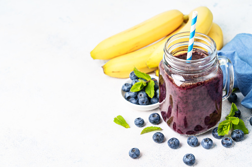 Blueberry banana smoothie in glass jar at blue background.