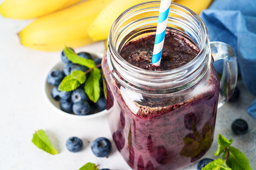 Blueberry banana smoothie in glass jar at white background. Close up.