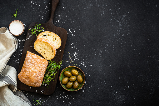 Ciabatta bread with olives and herbs on black. Mediterranean food. Top view with copy space.
