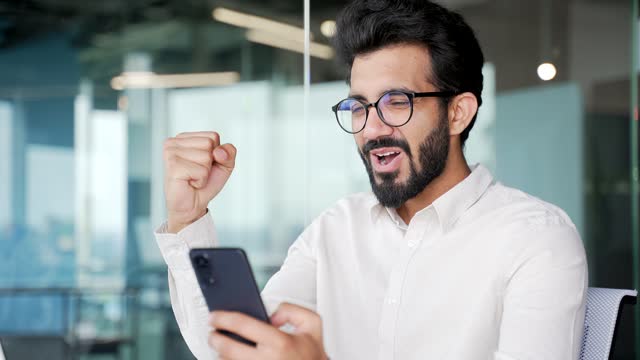 Close up Happy young businessman received great news on smartphone while sitting at workplace
