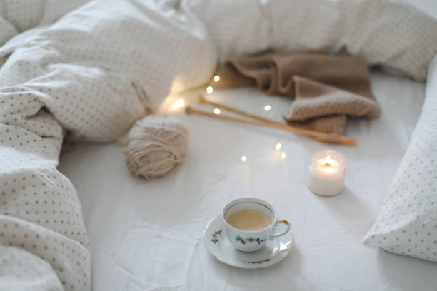 yarn and a cup of coffee on the bed. Hygge lifestyle, cozy mood. Handicraft day concept. acogedora naturaleza muerta matutina con una taza de café, vela, agujas y un hilo de lana en cama blanca. tejer suéter de lana cálido o vista superior de bufanda. estilo de vida hygge, estado de ánimo acogedor. concepto de día de artesanía.