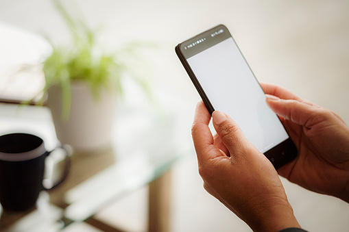 Unrecognizable woman using smartphone with blank screen at home