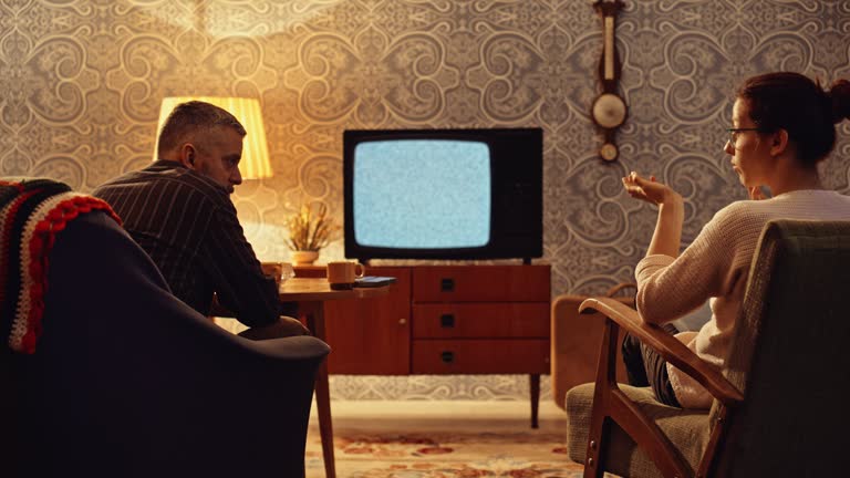 LD Couple sitting in the living room with an old tv with a snowy screen and talking