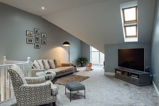 A wide view of a luxury modern living room area in a house in Gateshead, North East England. There is a sofa, armchair and TV in the room and windows bringing in the light.