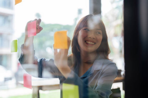 istock Thoughtful woman hand writing paper note, sticky note on glass window 1633388388