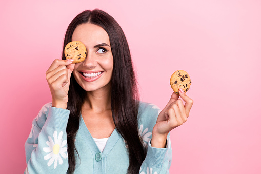 Photo of tricky cunning woman dressed blue cardigan cookie close eye looking empty space isolated pink color background.
