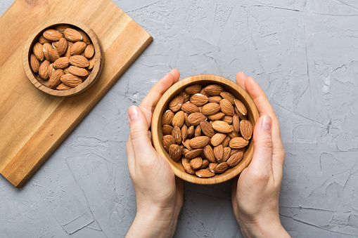 Woman hands holding a wooden bowl with almond nuts. Healthy food and snack. Vegetarian snacks of different nuts.