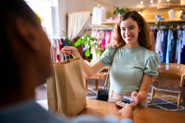 female customer in fashion store paying for clothes with contactless mobile phone payment app - detailhandel beroep fotos stockfoto's en -beelden