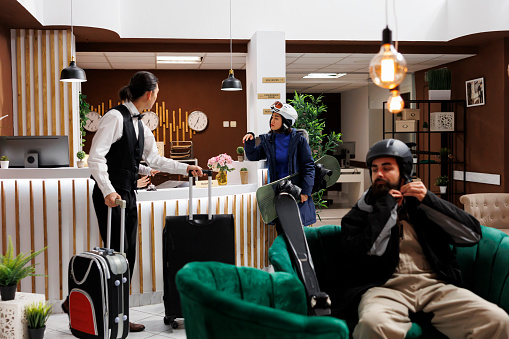 Arrival at modern hotel lobby, check-in, cozy lounge, luxury resort, winter gear, recreation, relaxation, exclusive holiday. Youthful tourists in lounge area awaiting accommodation.