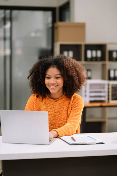 Business woman using laptop to work and writing on notebook with pen in office with mobile next to laptop.