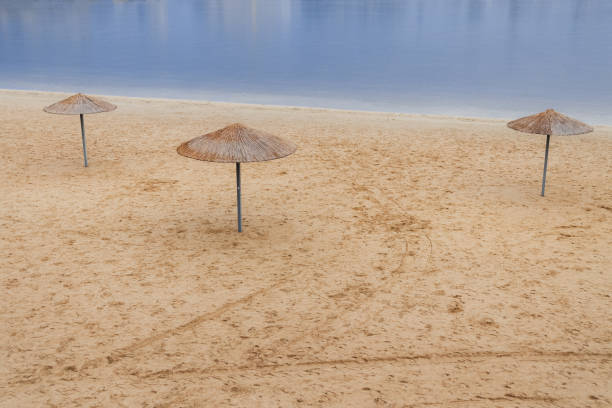 idyllic empty sand beach with three umbrella near shore line with smooth calm water surface space