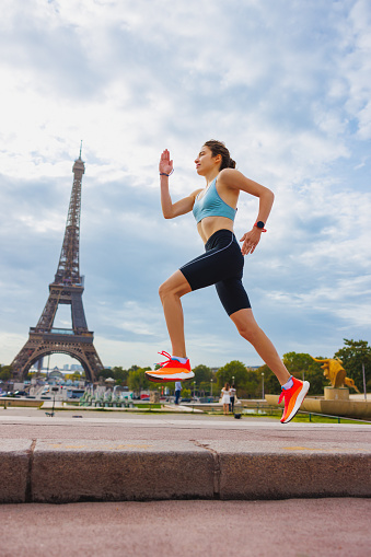 Young woman in sports outfit mid-air, running on a cloudy summer day in Paris, square near the Eiffel Tower