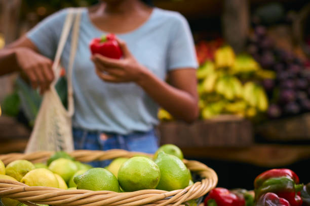 Primo piano del cliente femminile alla bancarella del mercato che sceglie il peperone rosso con i limoni in primo piano - foto stock