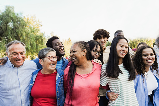 Group of multigenerational people smiling and laughing outdoor - Multiracial friends of different ages having fun together - Main focus on senor women face