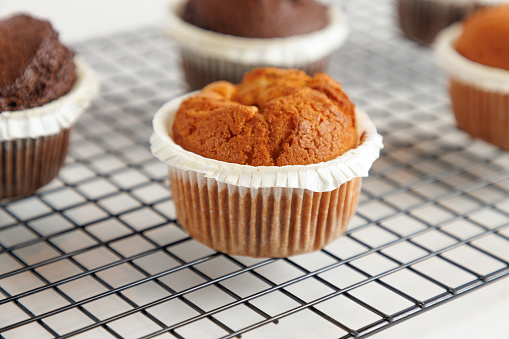 Close-up on baked muffin in wax paper cup, served on grid