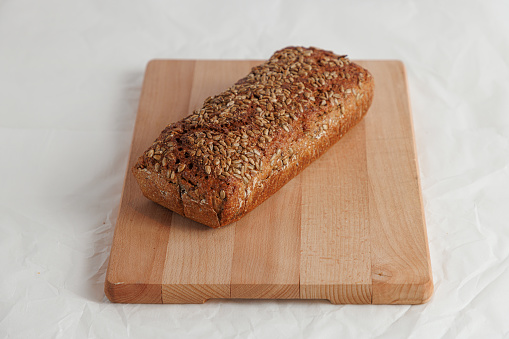 Baked loaf of dark bread with sunflower seed on crust, served on wooden board