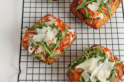 Puff pastry with tomato, arugula leaves and grated grana cheese on top served on grid