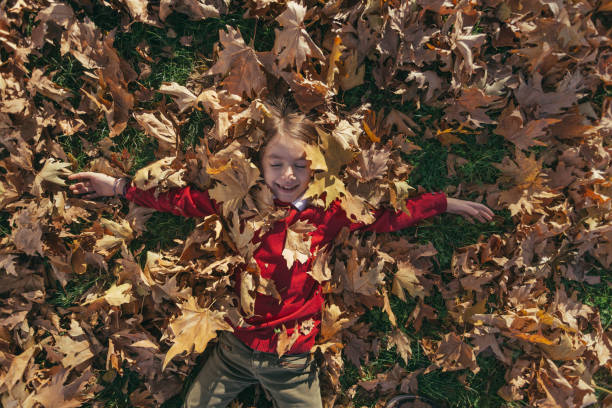 istock Cheerful little girl lying on back in dry maple leafs and enjoy 1633488031