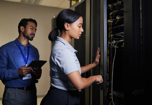 istock Server room, engineer teamwork and woman opening panel for maintenance or repairs at night. Cybersecurity, programmers and female with man holding tablet for software or networking in data center. 1633491374